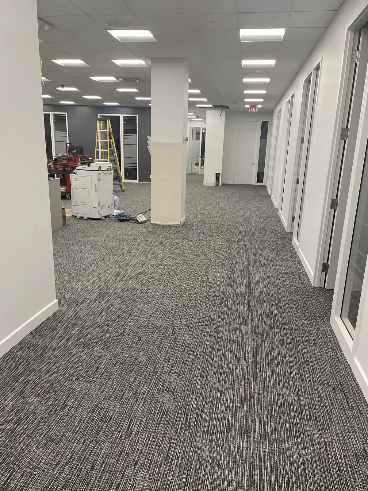 JT office common-area carpet tile during active fit-out, with tools and unfinished ceiling details visible