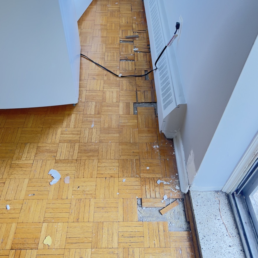 Missing and loose parquet pieces beside a radiator before repair on Dixon Road