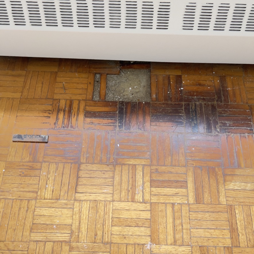 Open parquet section and damaged blocks below a radiator before repair