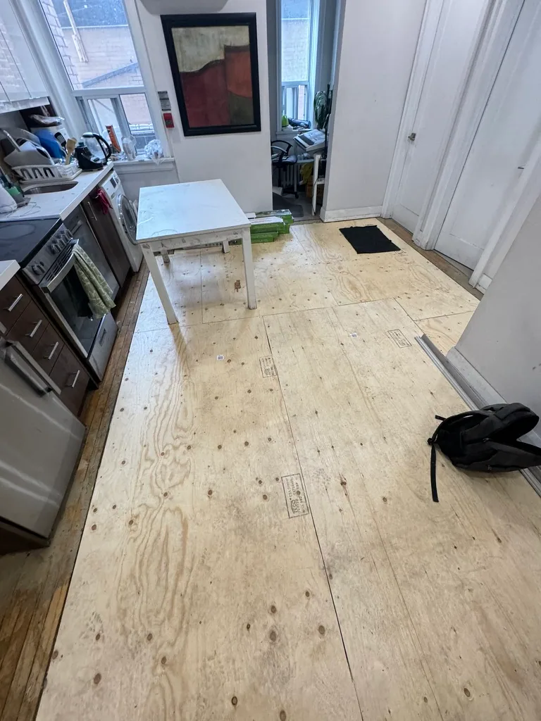 Wide view of new plywood subfloor preparation through the kitchen and hallway