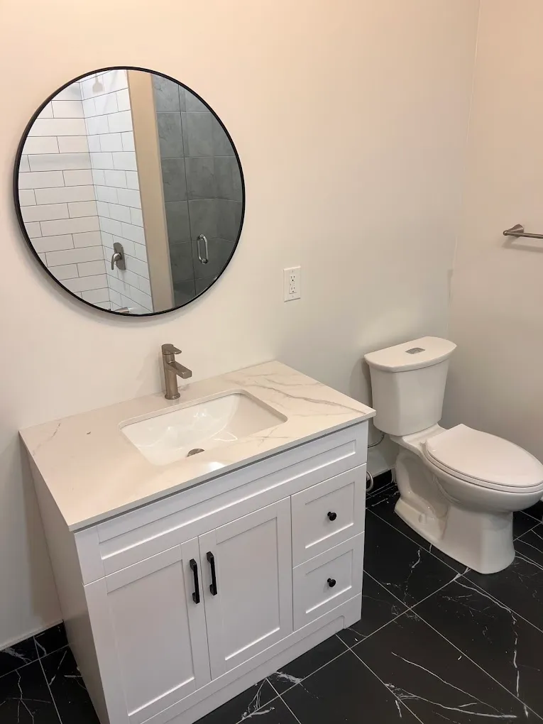 Finished bathroom vanity with black floor tile and round mirror