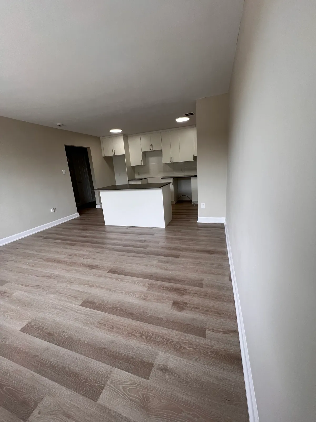 Wide finished living room leading to a white kitchen