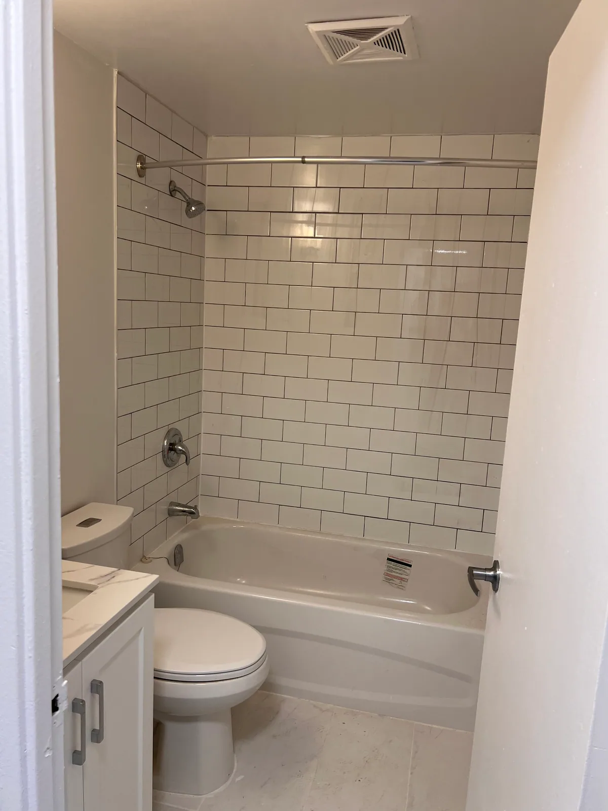 Completed compact bathroom with tiled tub surround and floor in Brampton