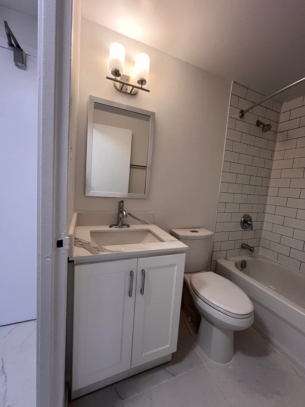Completed white bathroom vanity, mirror, lighting, toilet, and tub surround