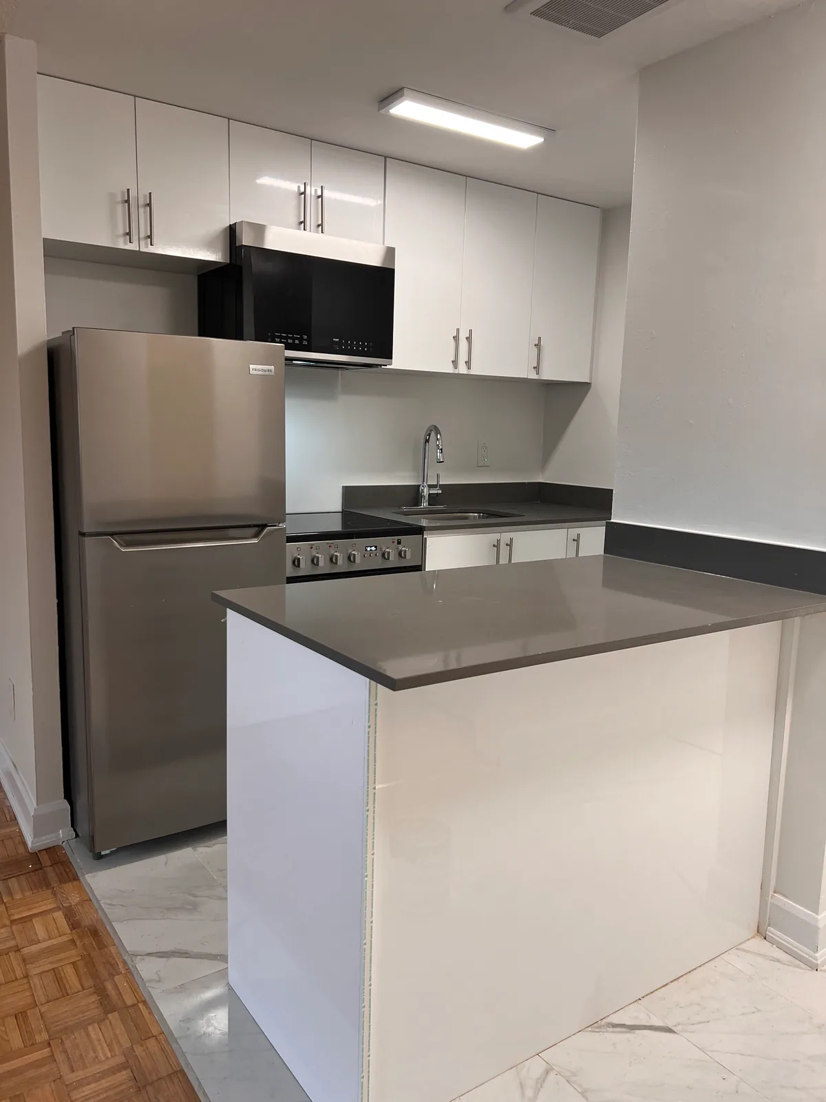 Completed Goreway kitchen with white upper cabinets, grey counter, sink, and stainless refrigerator