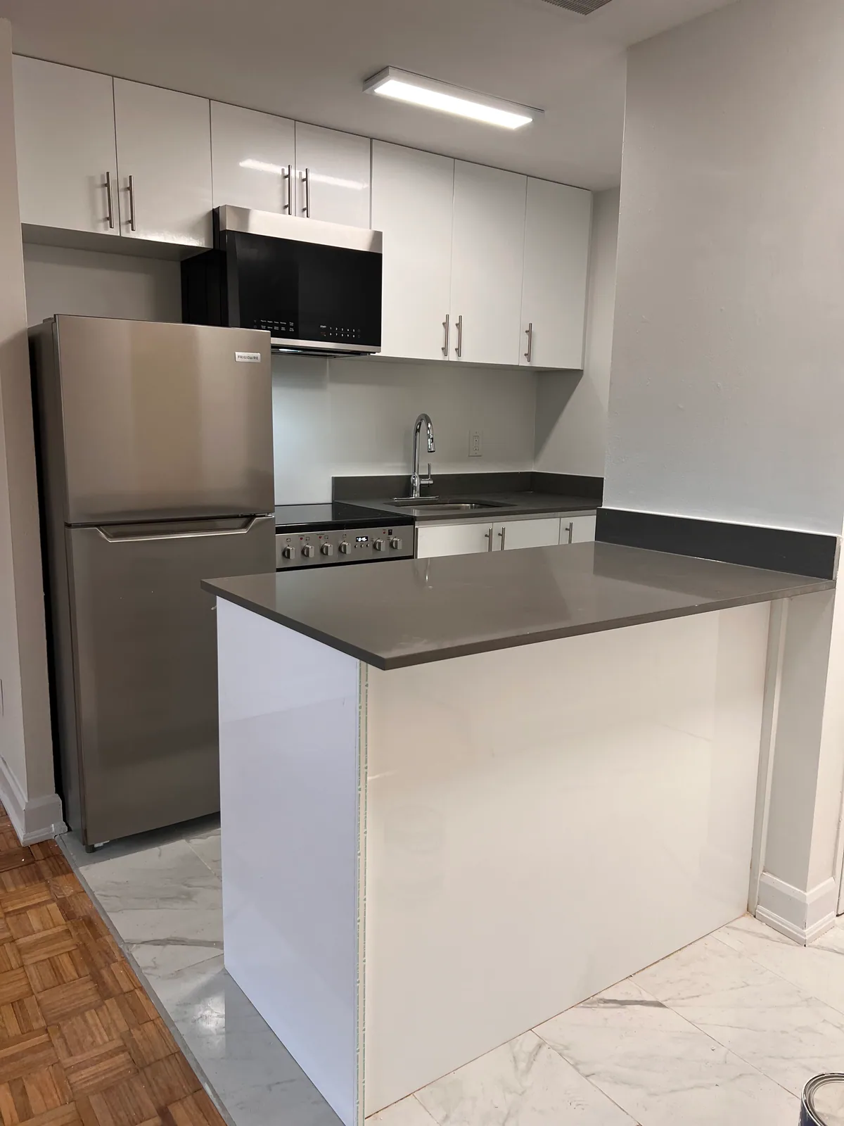 Grey peninsula and white cabinetry in completed Brampton condo kitchen