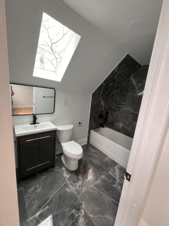 Finished skylight bathroom with dark marble-look tile, black vanity, and bathtub