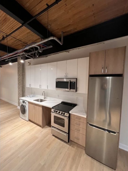 Finished loft kitchen with two-tone cabinets, stainless appliances, and wood flooring