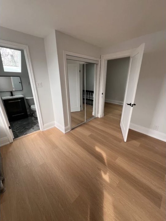 Renovated bedroom with light wood flooring, mirrored closet, and fresh paint
