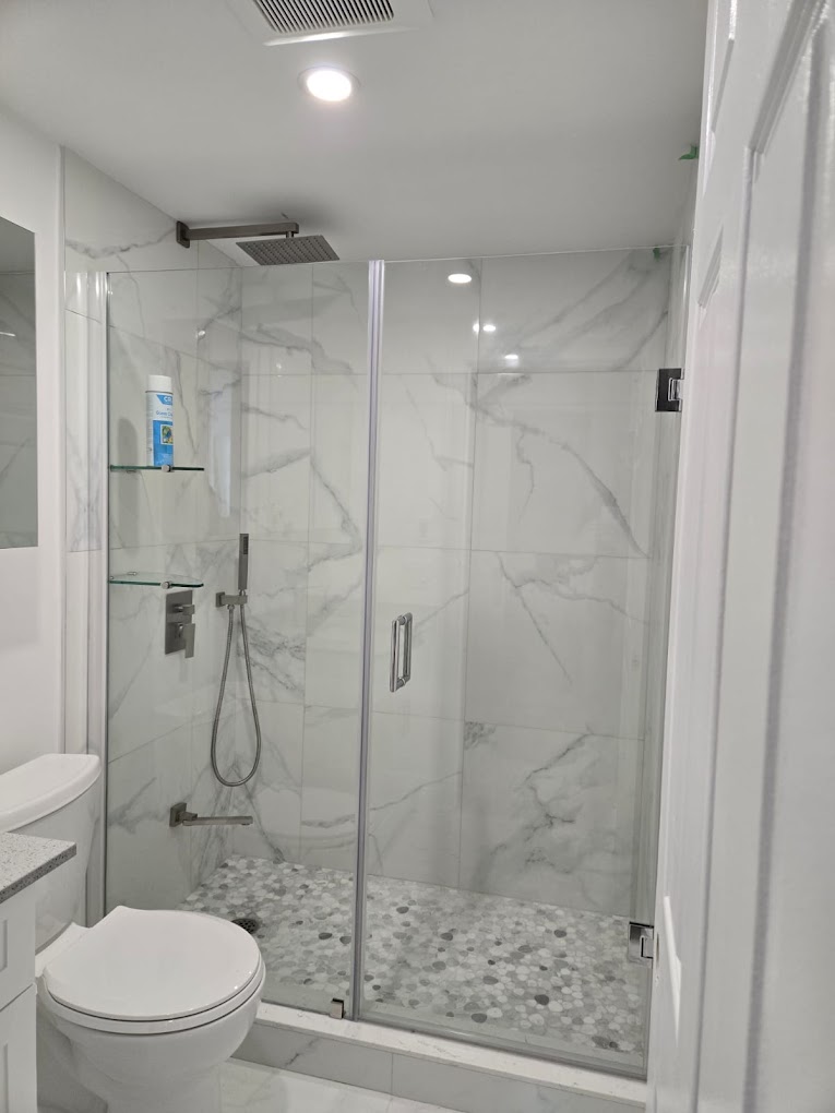 Completed walk-in shower with glass doors, marble-look wall panels, and mosaic floor tile