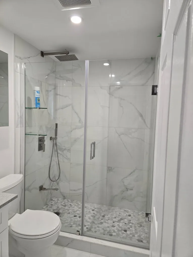 Completed walk-in shower with glass doors, marble-look wall panels, and mosaic floor tile