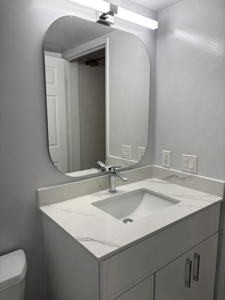 Bathroom vanity with white countertop, undermount sink, chrome faucet, and rounded mirror
