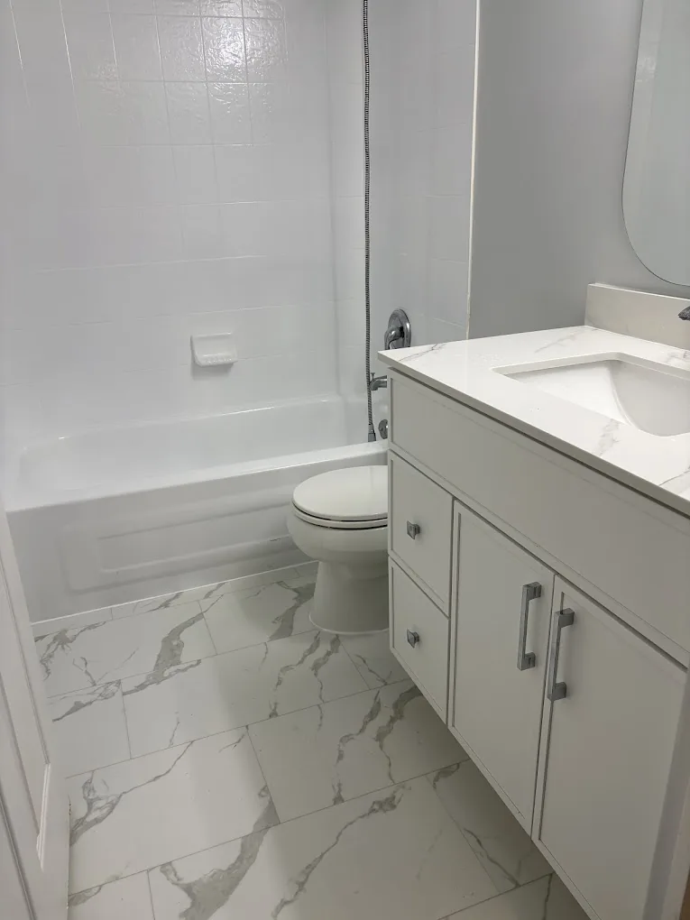 Bathroom with white tub surround, marble-look floor tile, vanity, and chrome fixtures