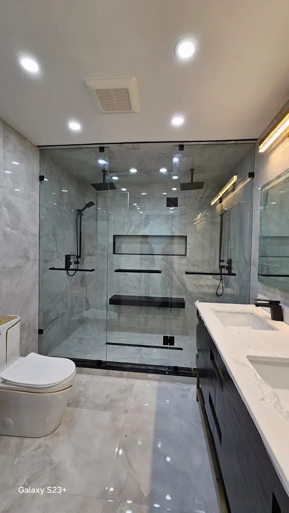 Modern bathroom with glass shower enclosure, large-format tile, and dark fixtures